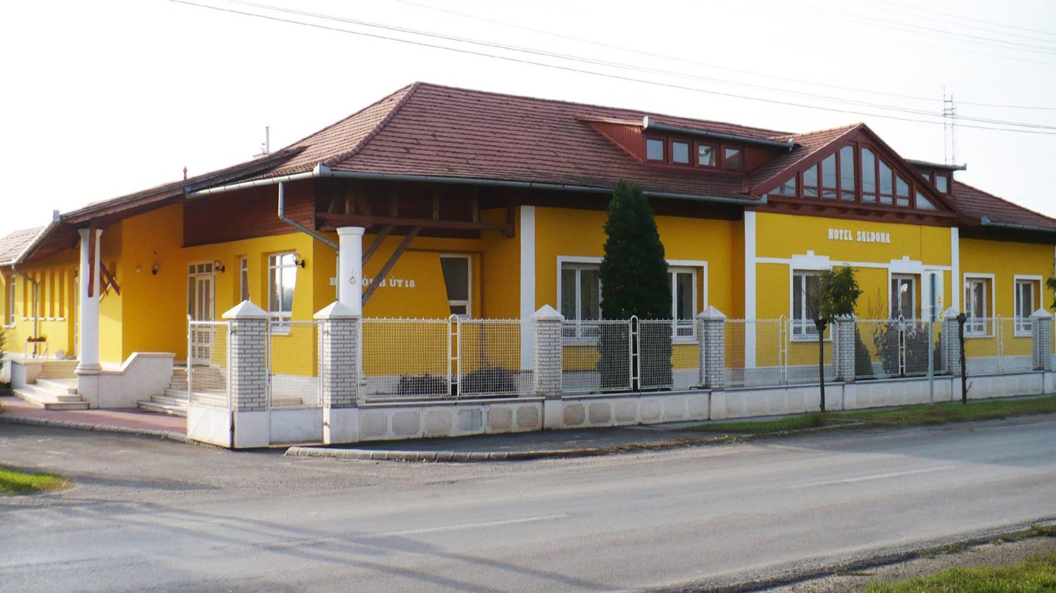 A Hotel Saldona sárga, cseréptetős épülete az utca felől, homlokzatán a Hotel Saldona felirattal és a kerítés mögötti előkerttel.